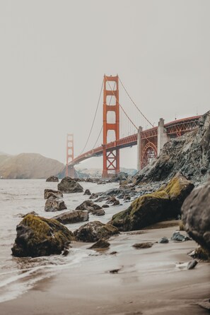 A coastal view with a prominent red bridge, rocky shoreline, and calm water. - Marin Suites Hotel (Corte Madera)