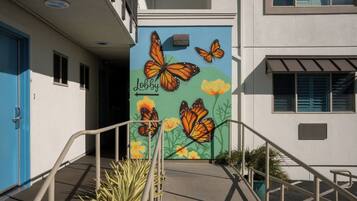 Un bâtiment orné d’une fresque représentant des papillons et des fleurs sur le côté, avec une porte bleue et un escalier menant à l’entrée.