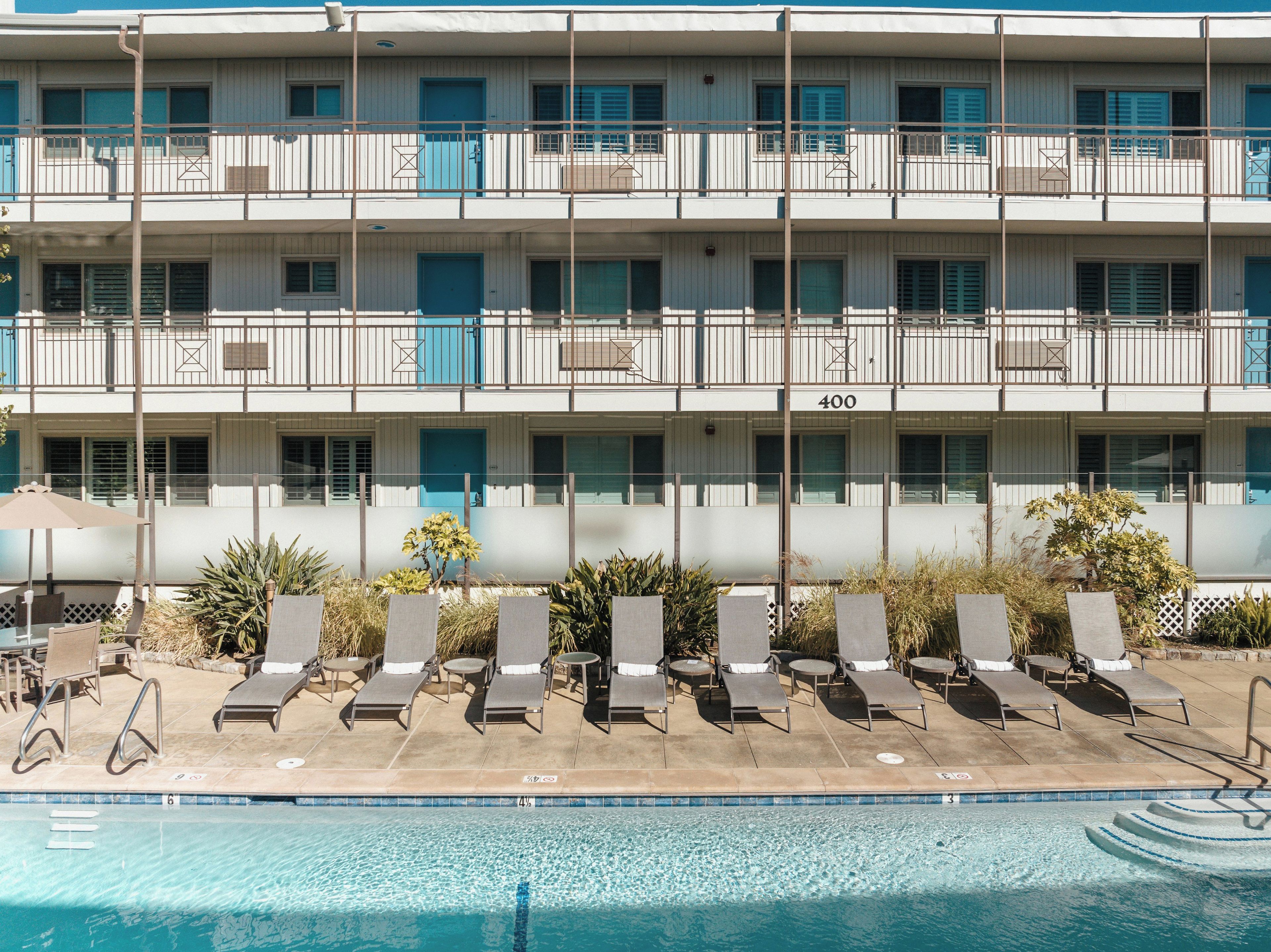 A multi-story hotel with a pool area, including sun loungers and a clear blue pool.