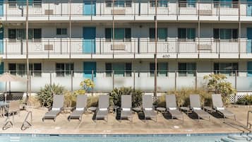 A multi-story hotel with a pool area, including sun loungers and a clear blue pool.