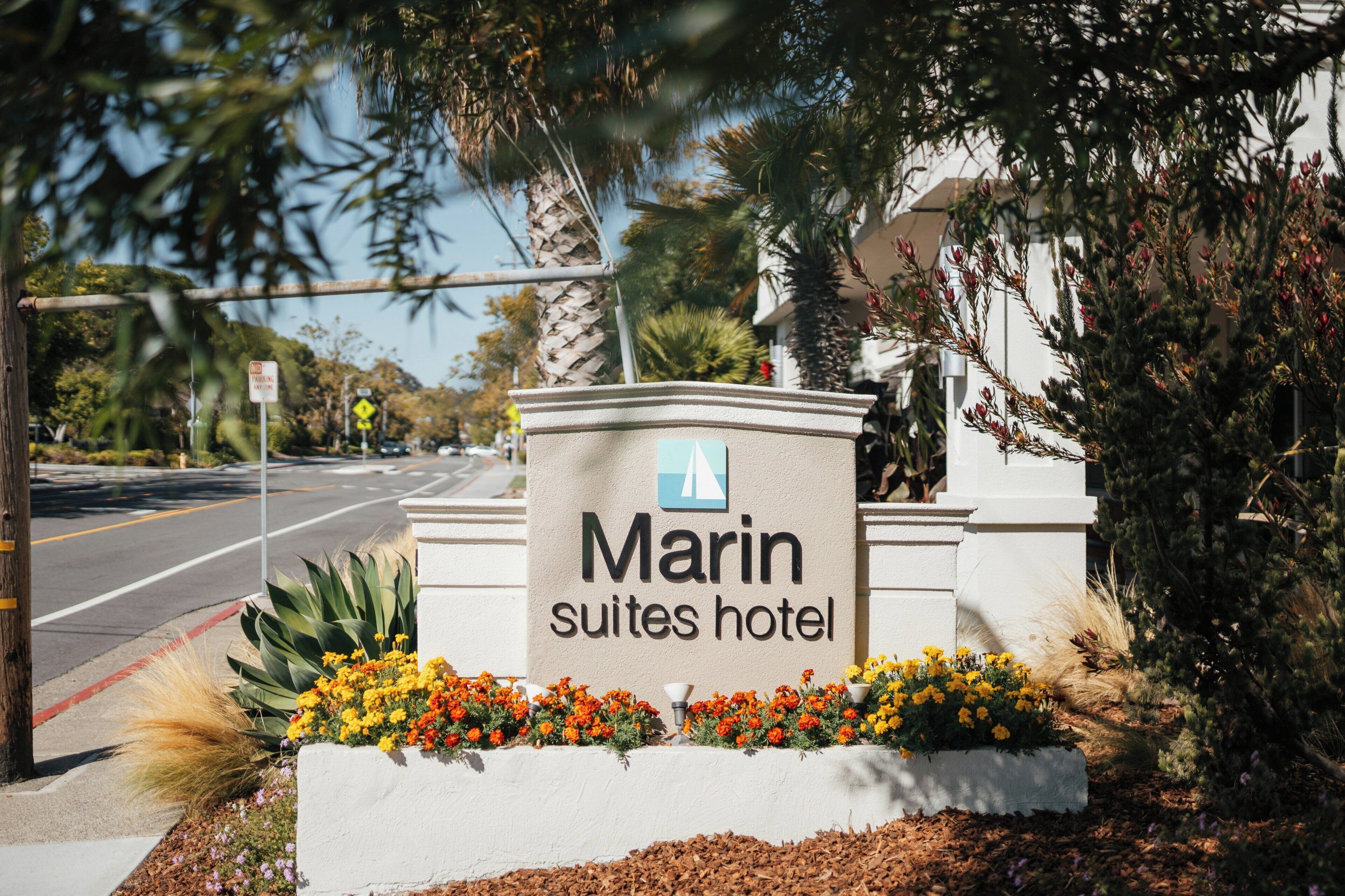 A sign for Marin Suites Hotel with a clear view of the road and surrounding vegetation.