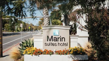 A sign for Marin Suites Hotel with a clear view of the road and surrounding vegetation.