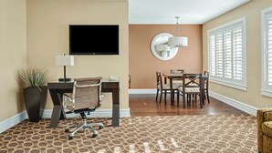 Una sala de estar moderna con un televisor de pantalla plana, un comedor con mesa y sillas, una planta en maceta y una alfombra estampada.