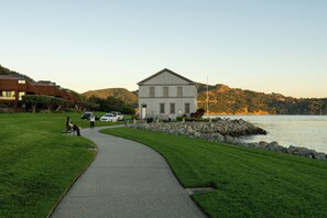 A pathway leading to a white building with a gabled roof, surrounded by a grassy area and a body of water. - Marin Suites Hotel (Corte Madera)