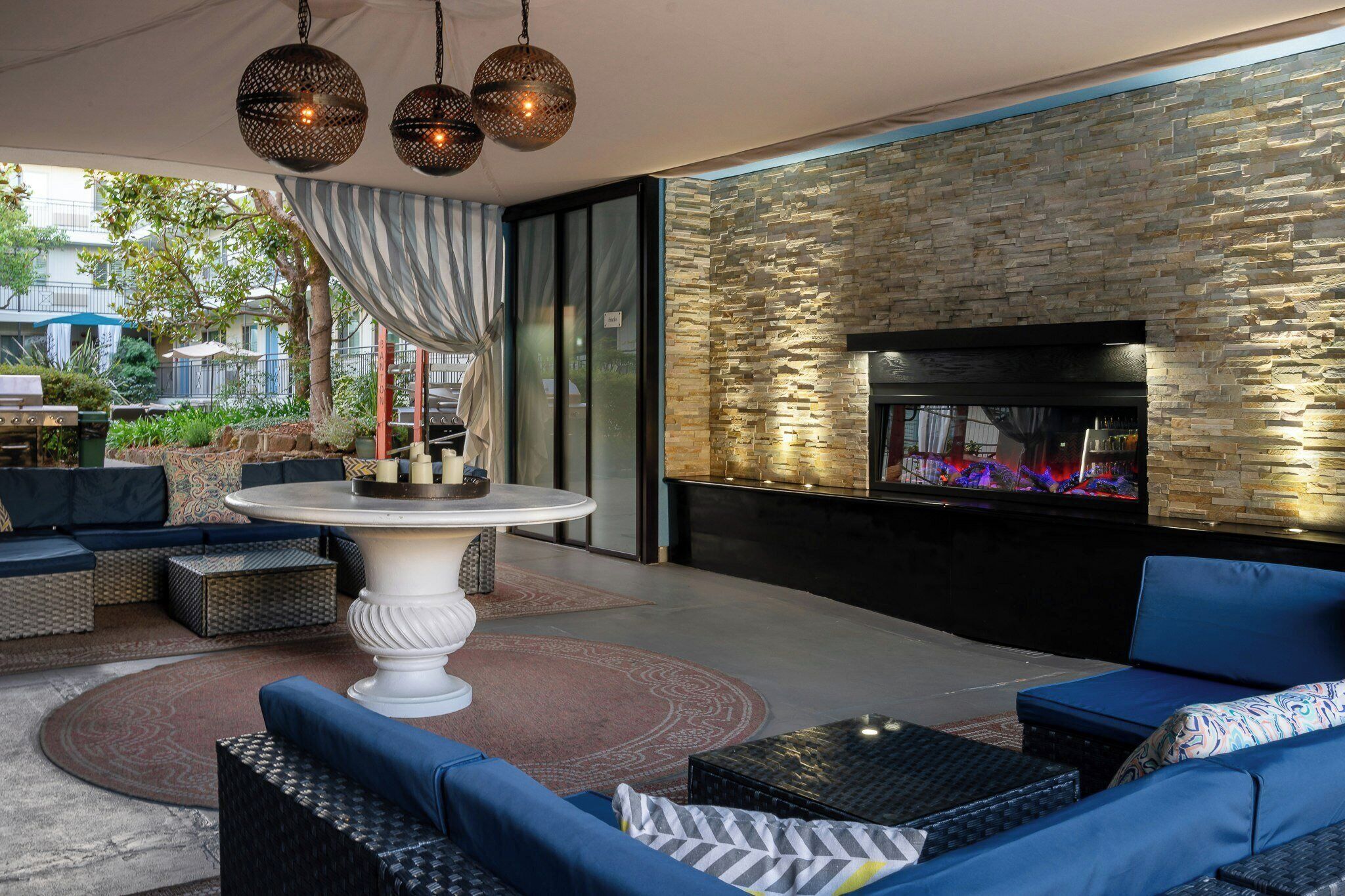 An outdoor patio with a round table, sofas, and a stone wall with a fireplace.