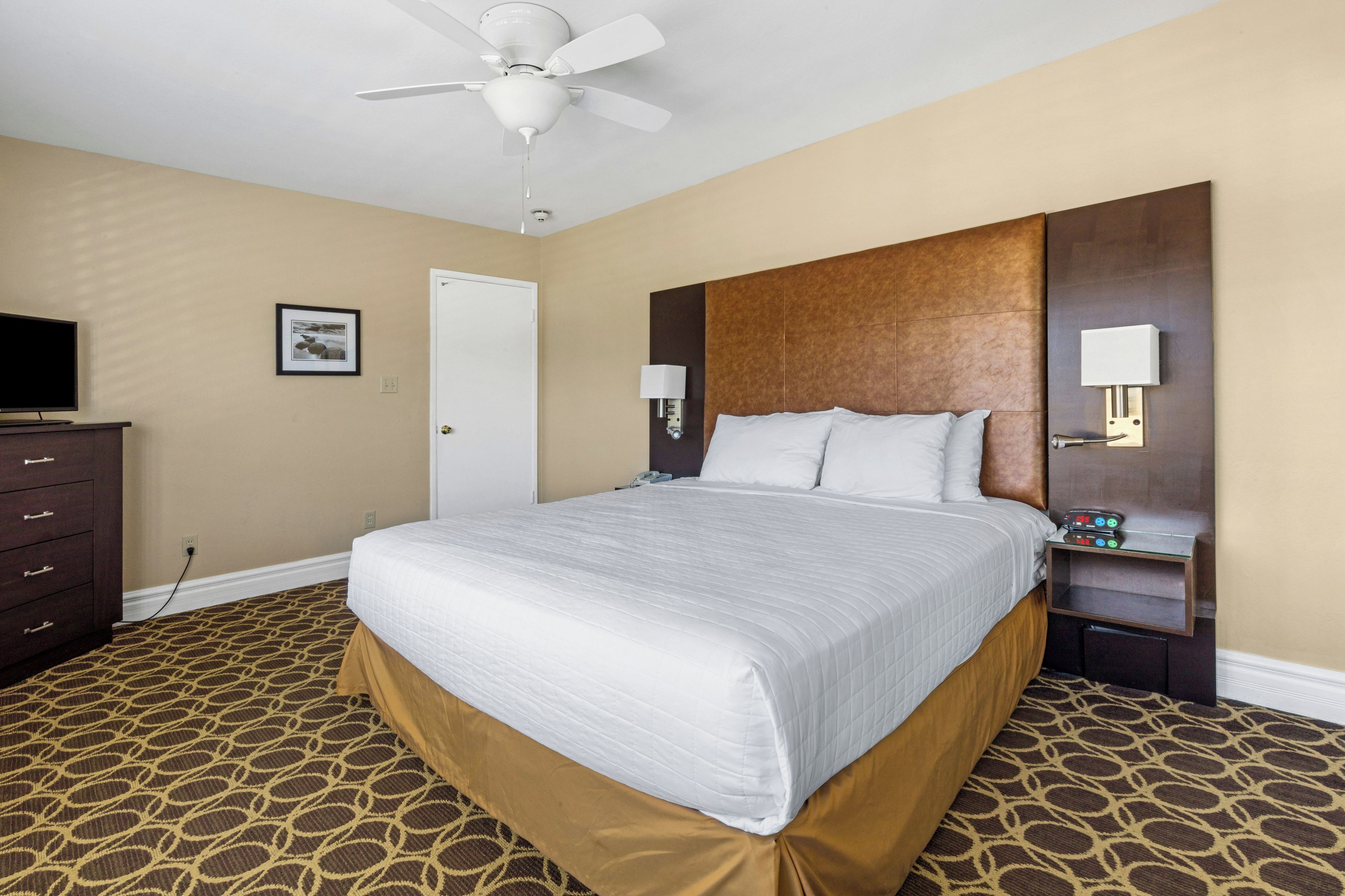 Une chambre d’hôtel équipée d’un lit, d’une commode, d’une télévision et d’un ventilateur de plafond.