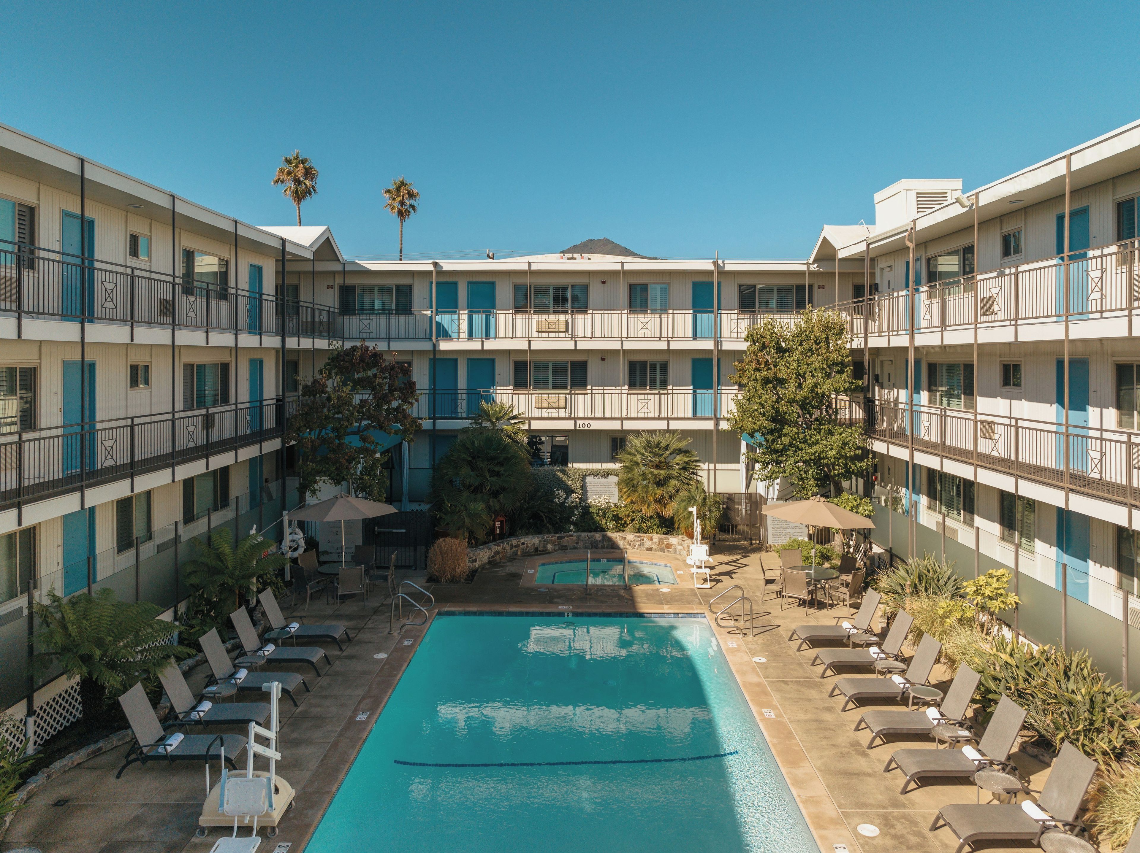 A hotel with a central swimming pool, multiple balconies, and outdoor seating areas.