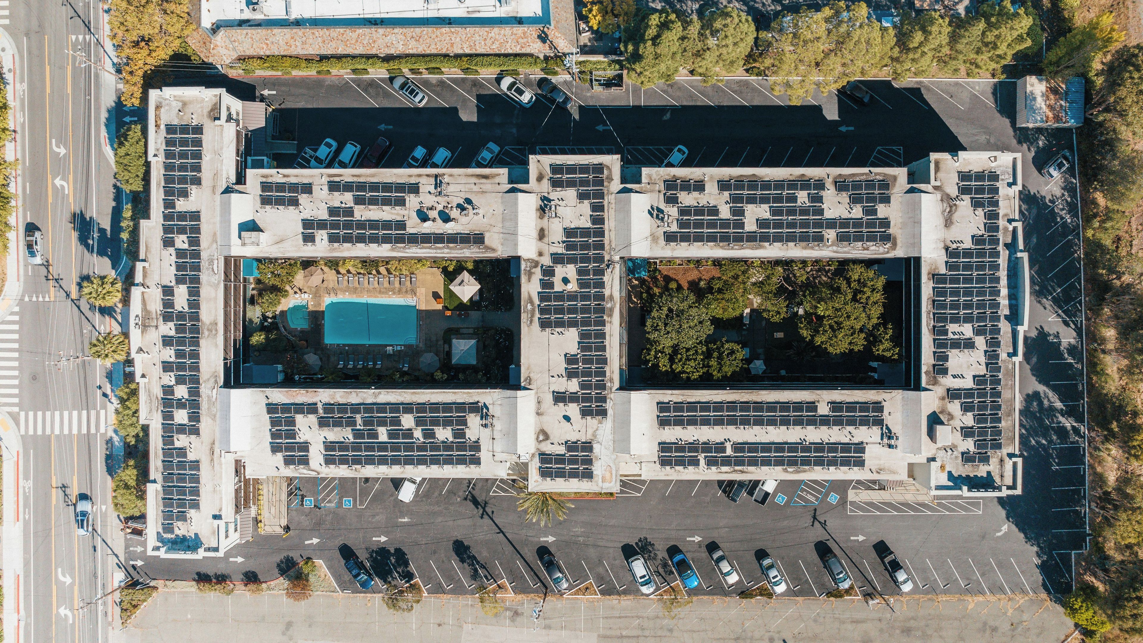 An aerial view of a parking lot with multiple rows of parked cars, a central landscaped area, and a building with a flat roof.