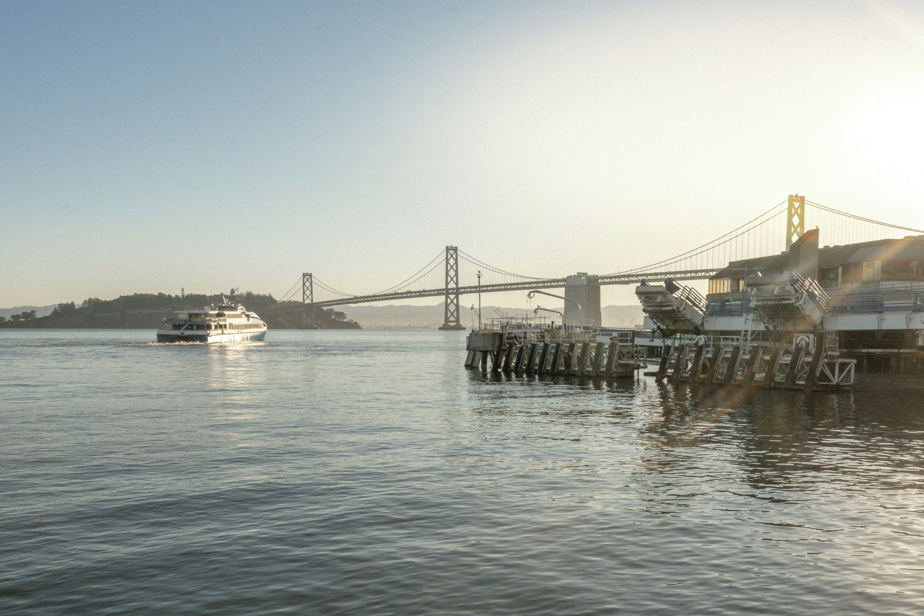 A ferry crossing a bridge over calm water with a cityscape in the background.