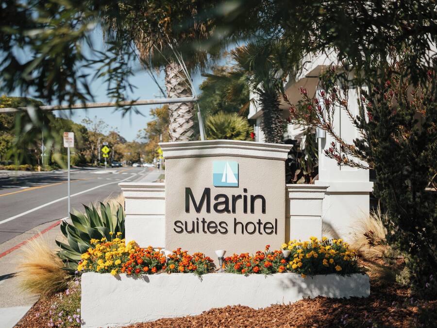 Schild für das Marin Suites Hotel, mit freier Sicht auf die Straße und die umliegende Vegetation.