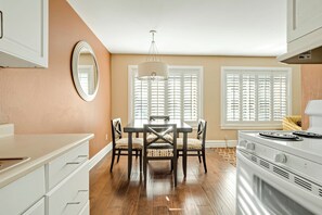A kitchen with a dining table, chairs, a stove, and a large window with blinds. - Marin Suites Hotel (Corte Madera)