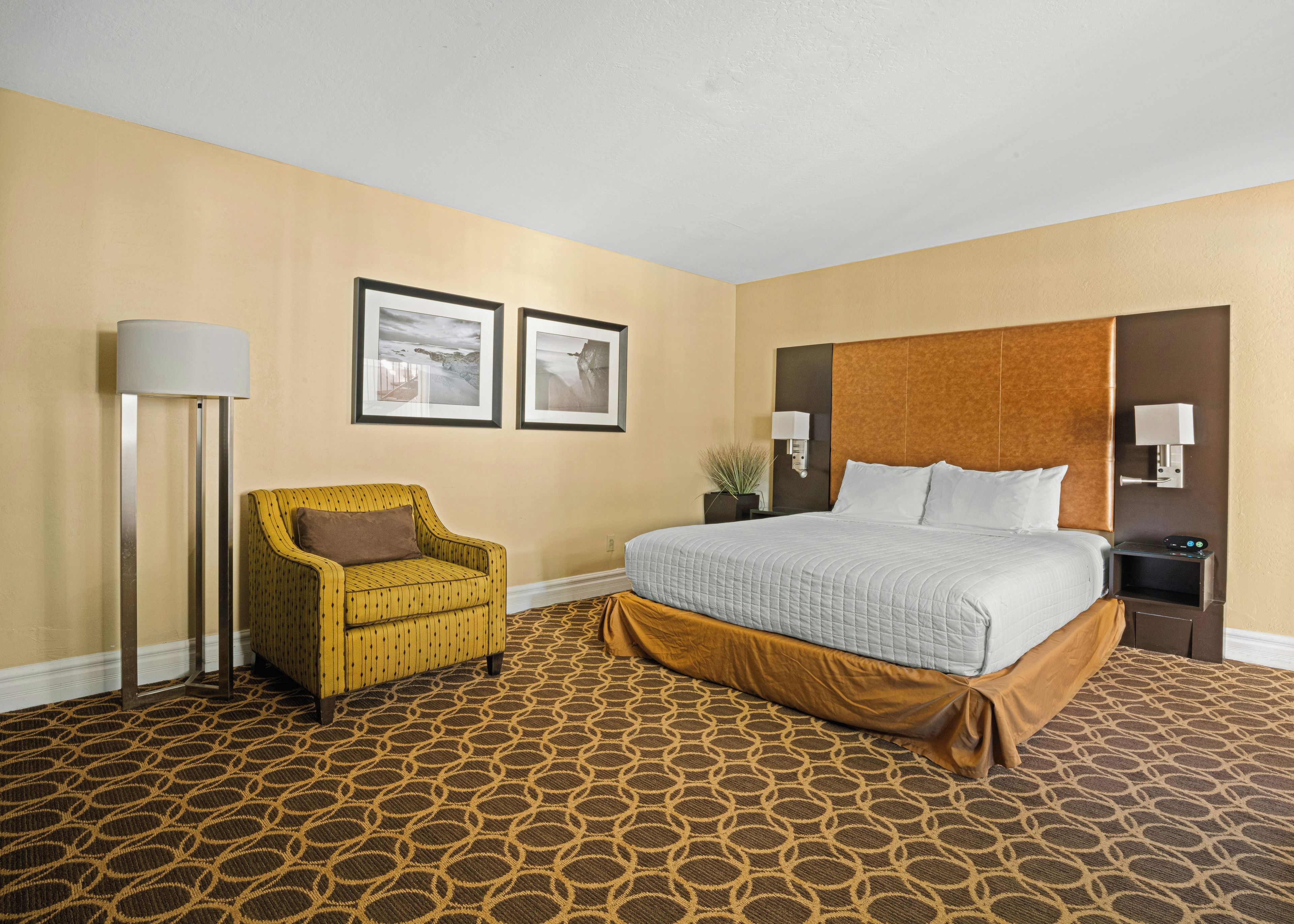 A hotel room with a bed, a chair, a lamp, and two framed pictures on the wall.