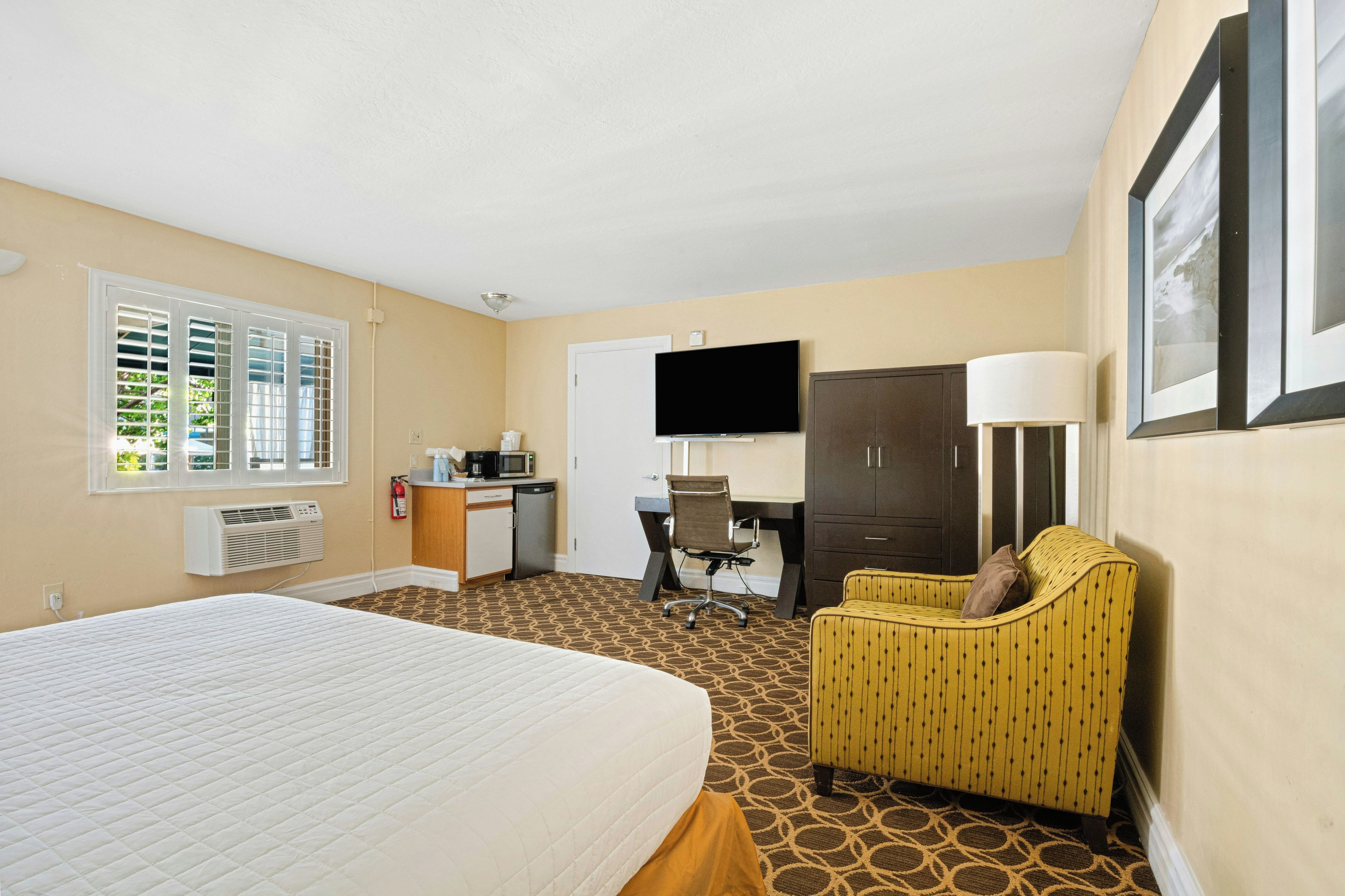 A hotel room with a bed, a desk, a chair, a television, and a wardrobe.