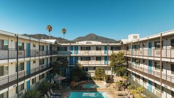 A hotel with a central pool, multiple balconies, and a mountain view.