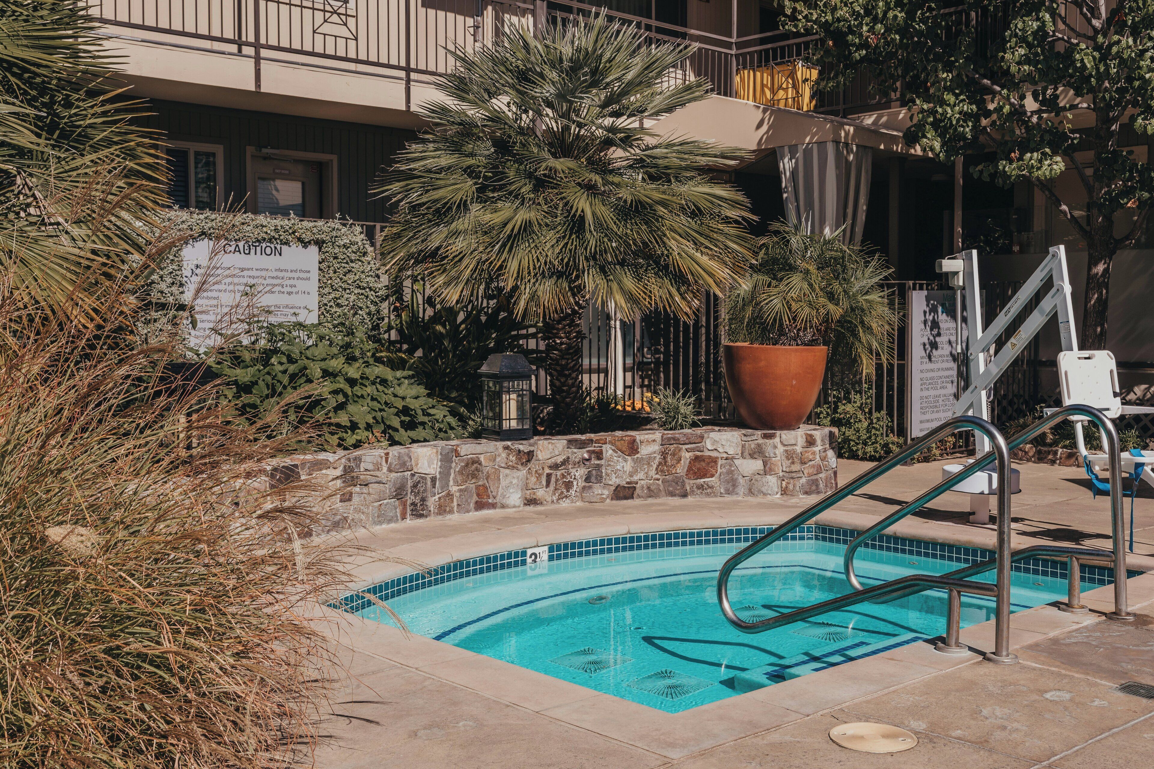 A swimming pool with a stone border, surrounded by potted plants and a sign with text.