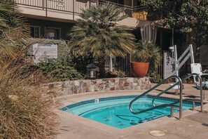 A swimming pool with a stone border, surrounded by potted plants and a sign with text. - Marin Suites Hotel (Corte Madera)