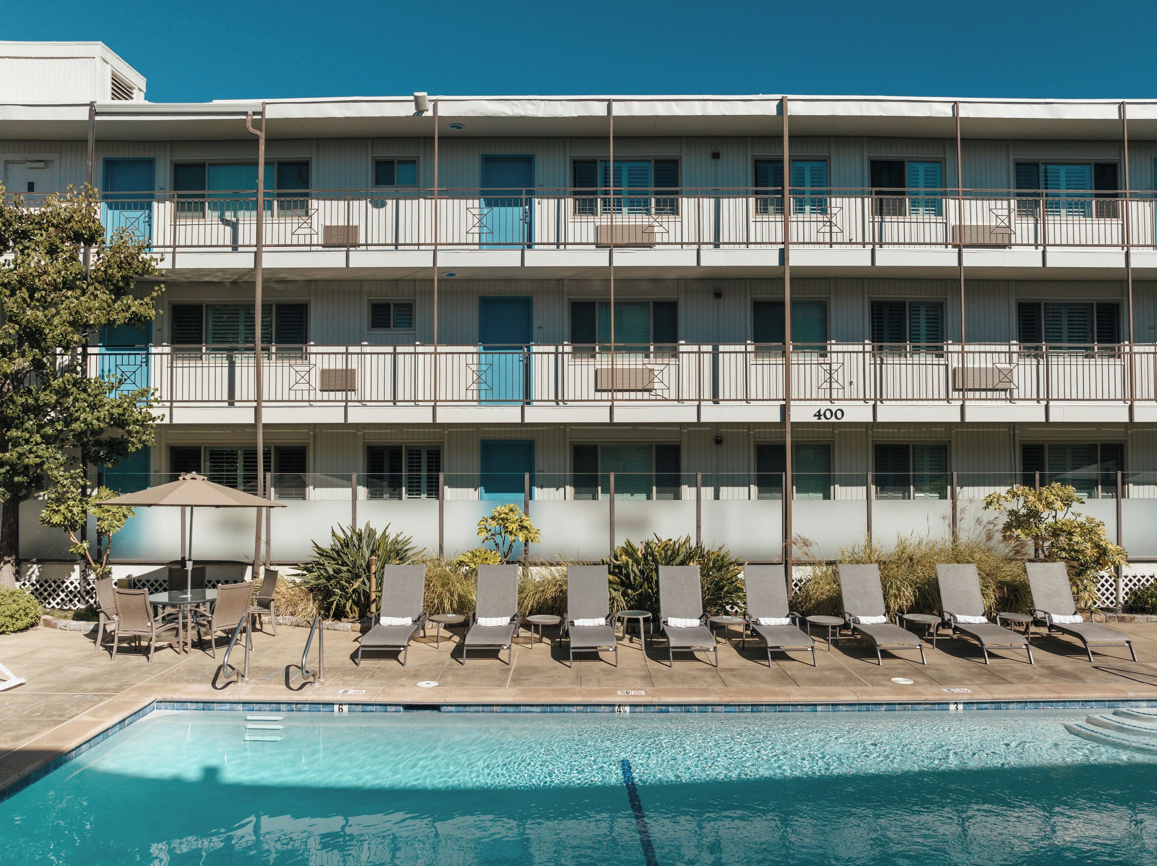A multi-story hotel with a swimming pool, outdoor seating, and a balcony with a view.