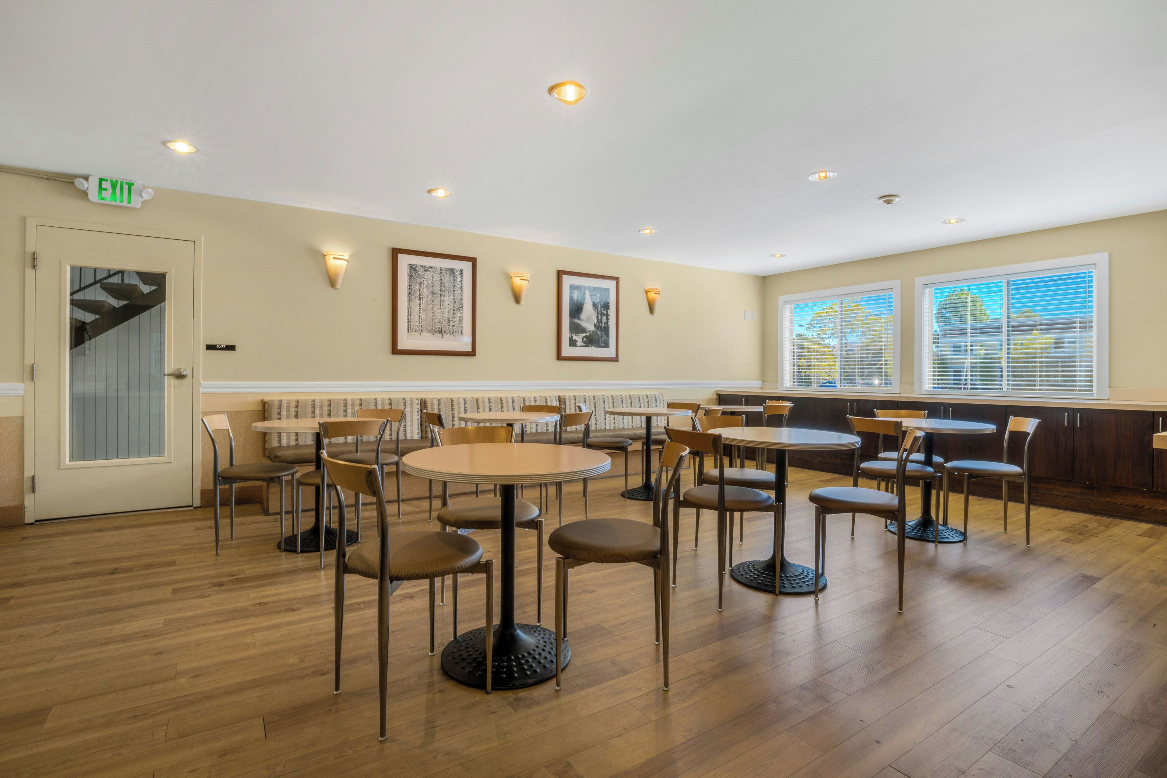 A restaurant with multiple tables and chairs, a staircase, and framed artwork on the walls.