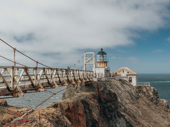 A coastal lighthouse with a metal bridge leading to it, overlooking the sea.