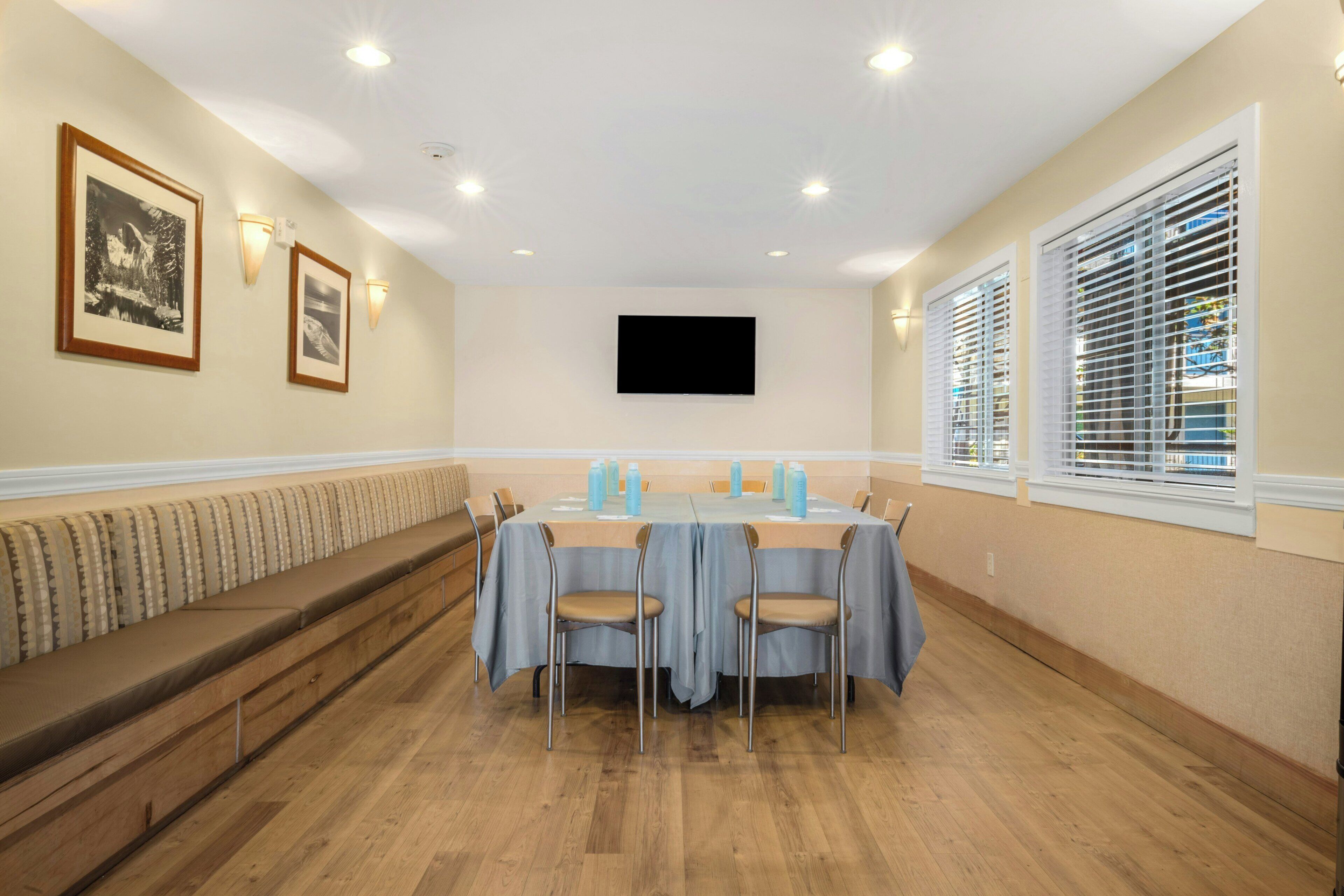 A conference room with a long table, chairs, a bench, and a flat-screen TV on the wall.