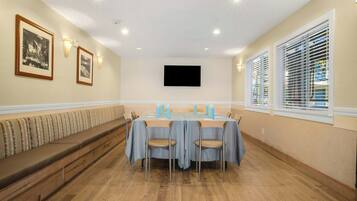 A conference room with a long table, chairs, a bench, and a flat-screen TV on the wall.