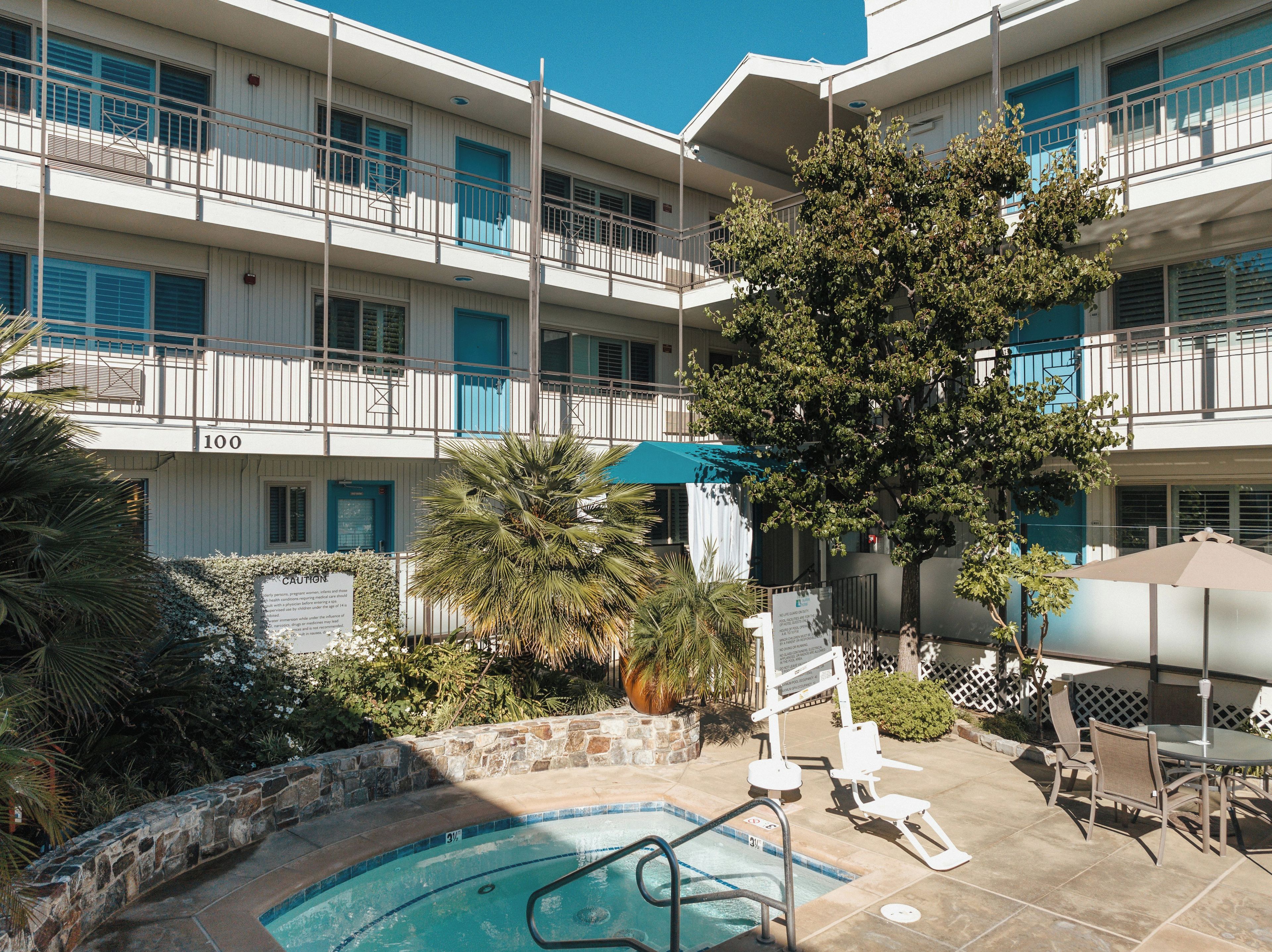 A multi-story hotel with a pool area, outdoor seating, and a tree.