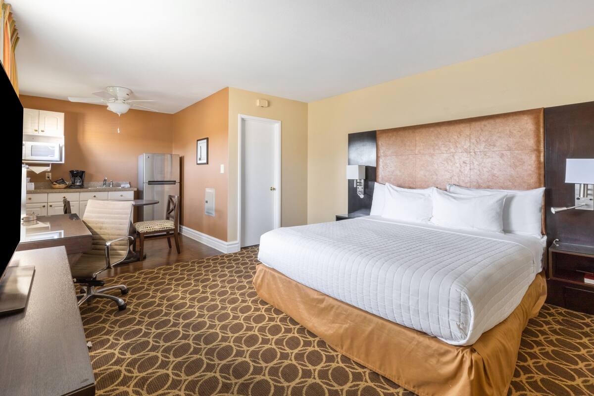A hotel room with a large bed, a desk with a chair, a microwave, a refrigerator, and a ceiling fan.