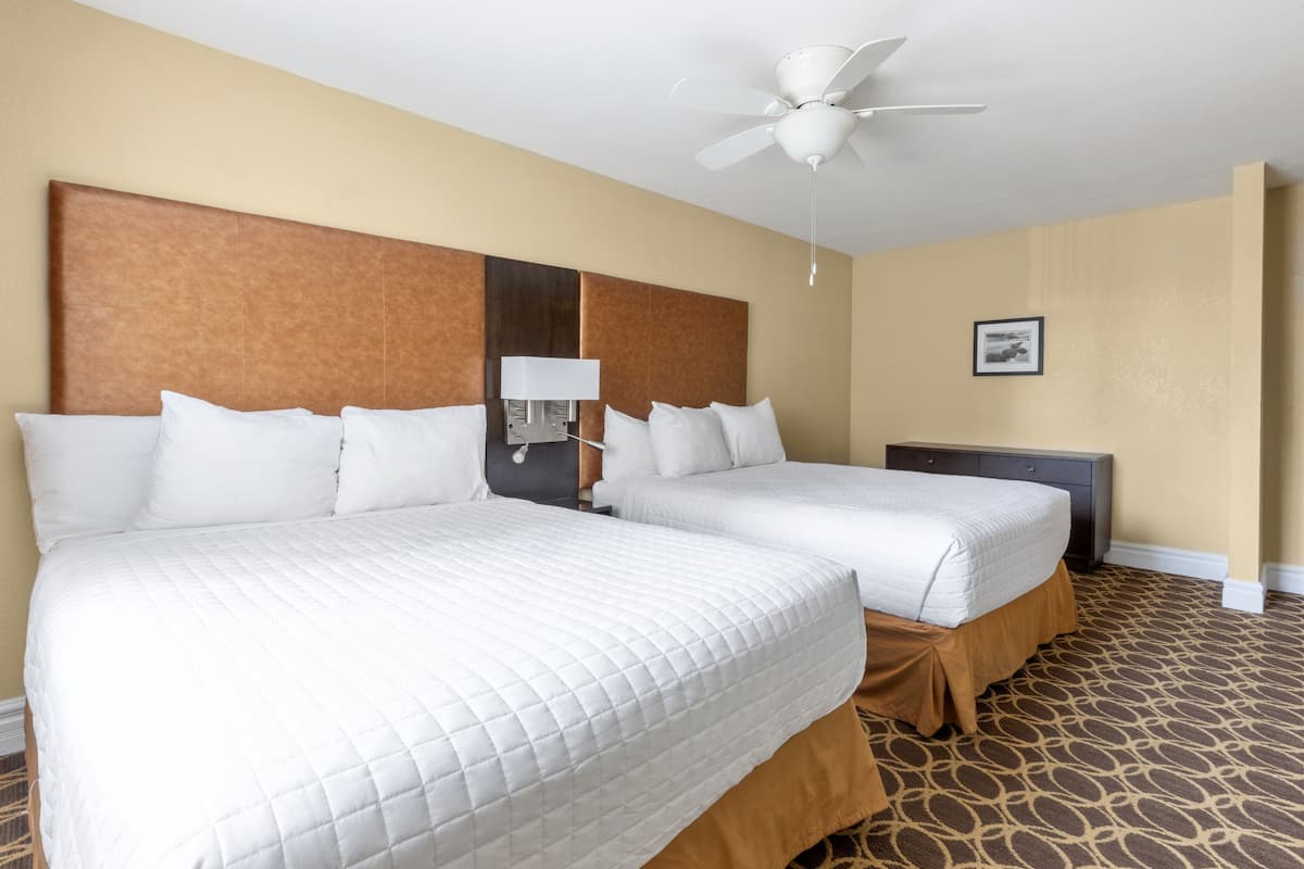 A hotel room with two queen beds, a ceiling fan, a bedside table with a lamp, and a framed picture on the wall.