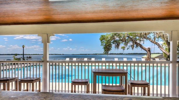 A poolside area with a view of the water, wooden furniture, and a white fence.