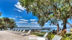 A waterfront patio with lounge chairs and a table, overlooking a body of water and a dock.