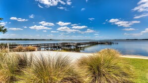 A wooden pier extending into a calm lake, surrounded by grassy areas and a clear sky.