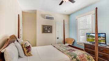 Un dormitorio con cama, ventilador de techo, ventana con persianas, televisión y cómoda.