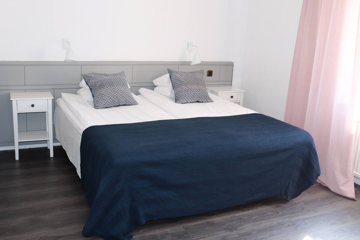 A neatly made bed with a dark blue bedspread, two pillows, and two bedside tables with lamps.