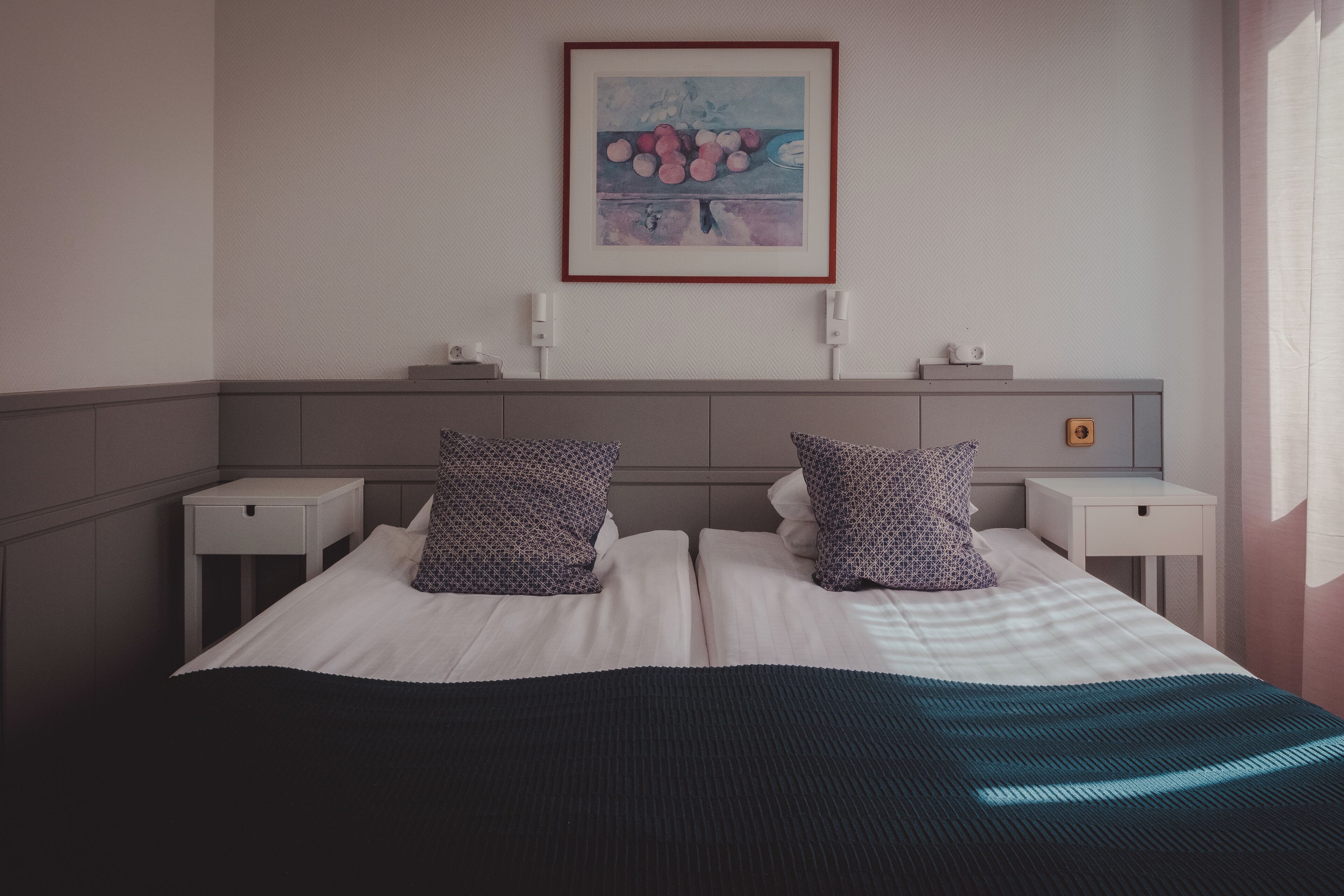A neatly made bed with a black and blue striped blanket, two white nightstands, a framed artwork on the wall, and a small bedside table with a lamp.