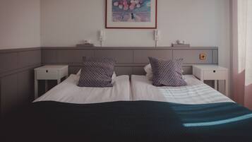 A neatly made bed with a black and blue striped blanket, two white nightstands, a framed artwork on the wall, and a small bedside table with a lamp.