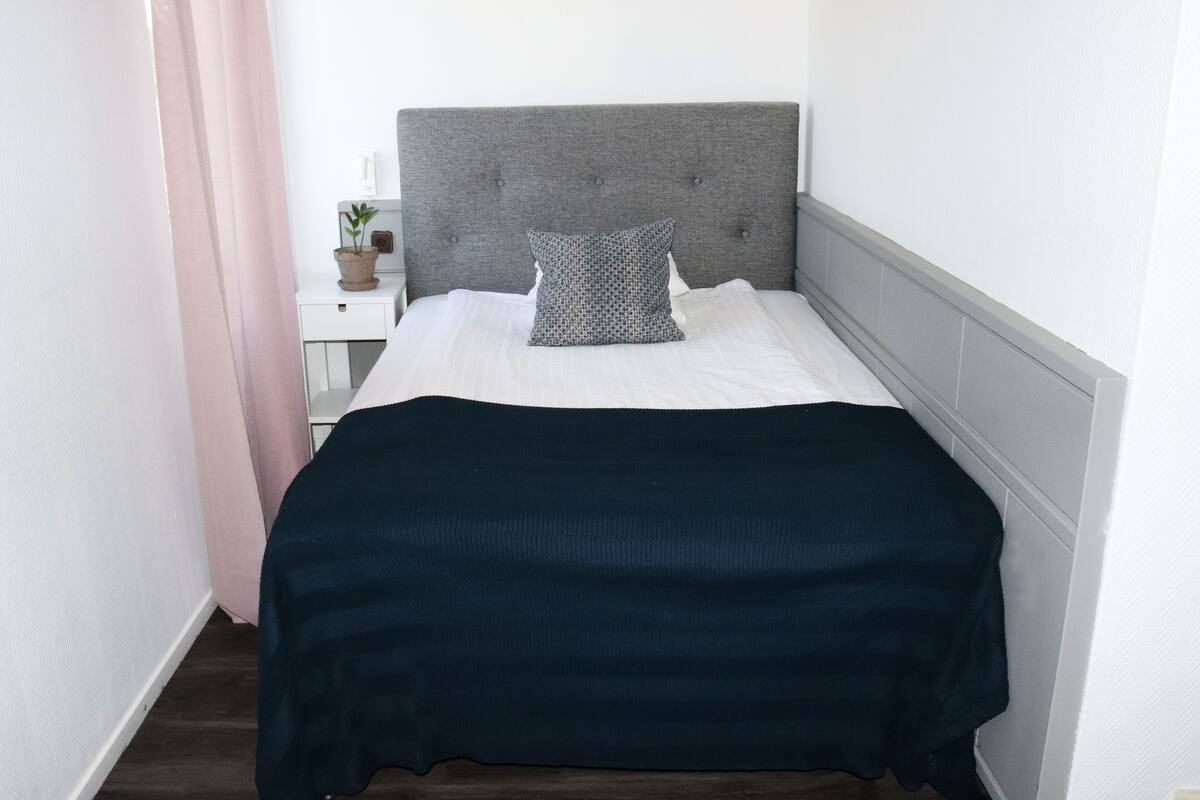 A neatly made bed with a grey headboard, a white pillow, and a dark blue blanket.