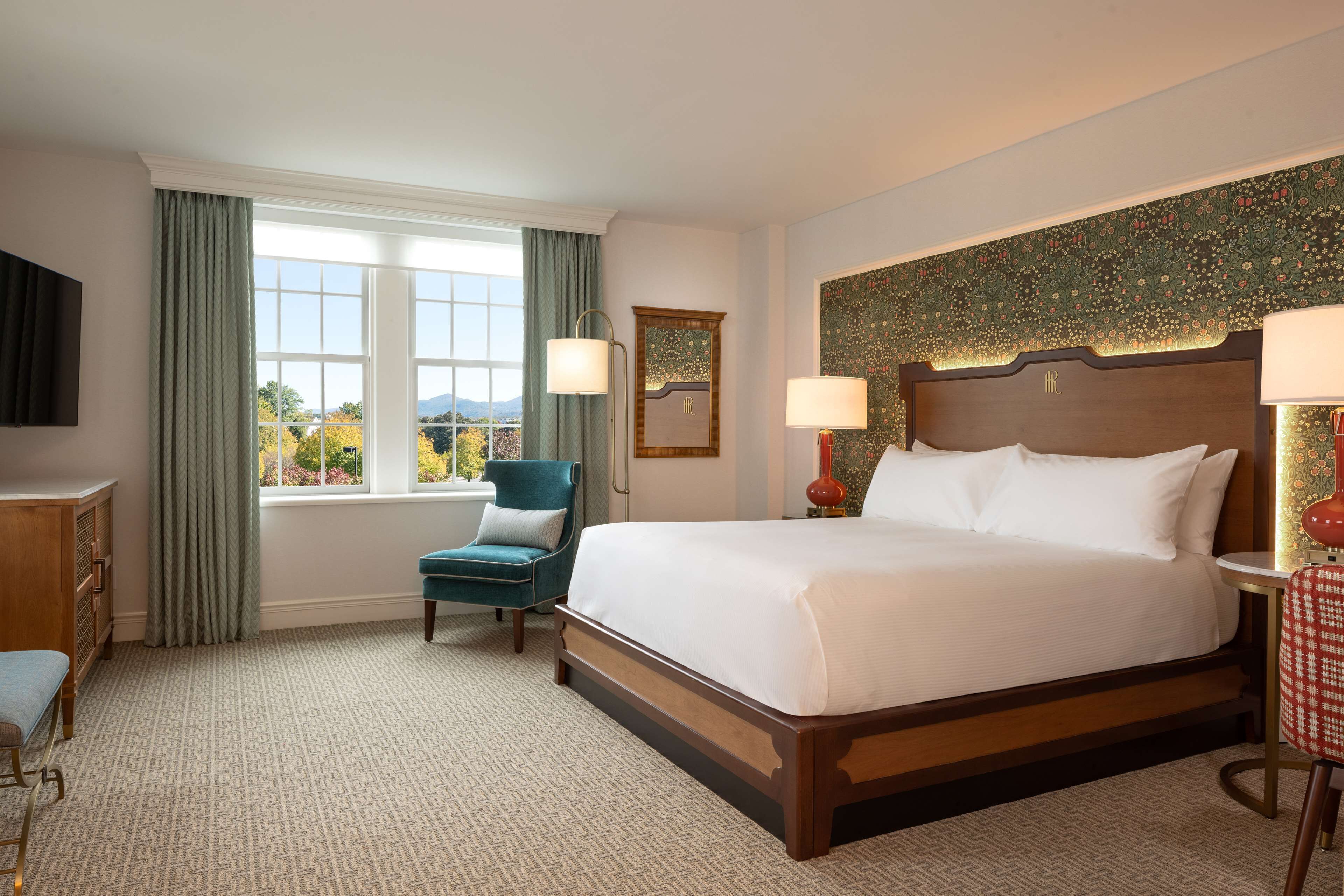 Quarto de hotel com uma cama grande, uma escrivaninha, uma cadeira e uma janela com cortinas.