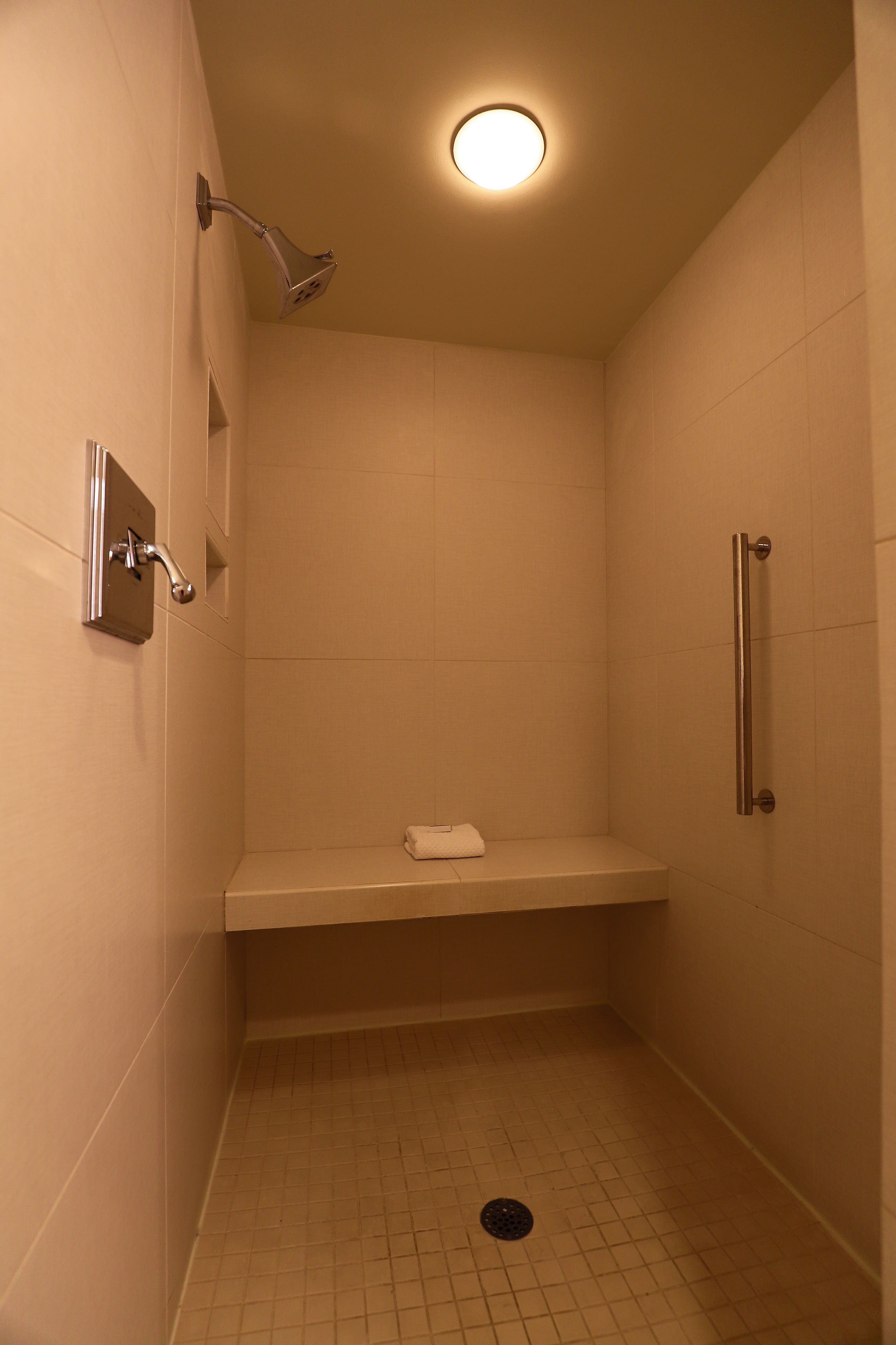 A small, enclosed shower area with a bench, a handheld showerhead, and a grab bar.