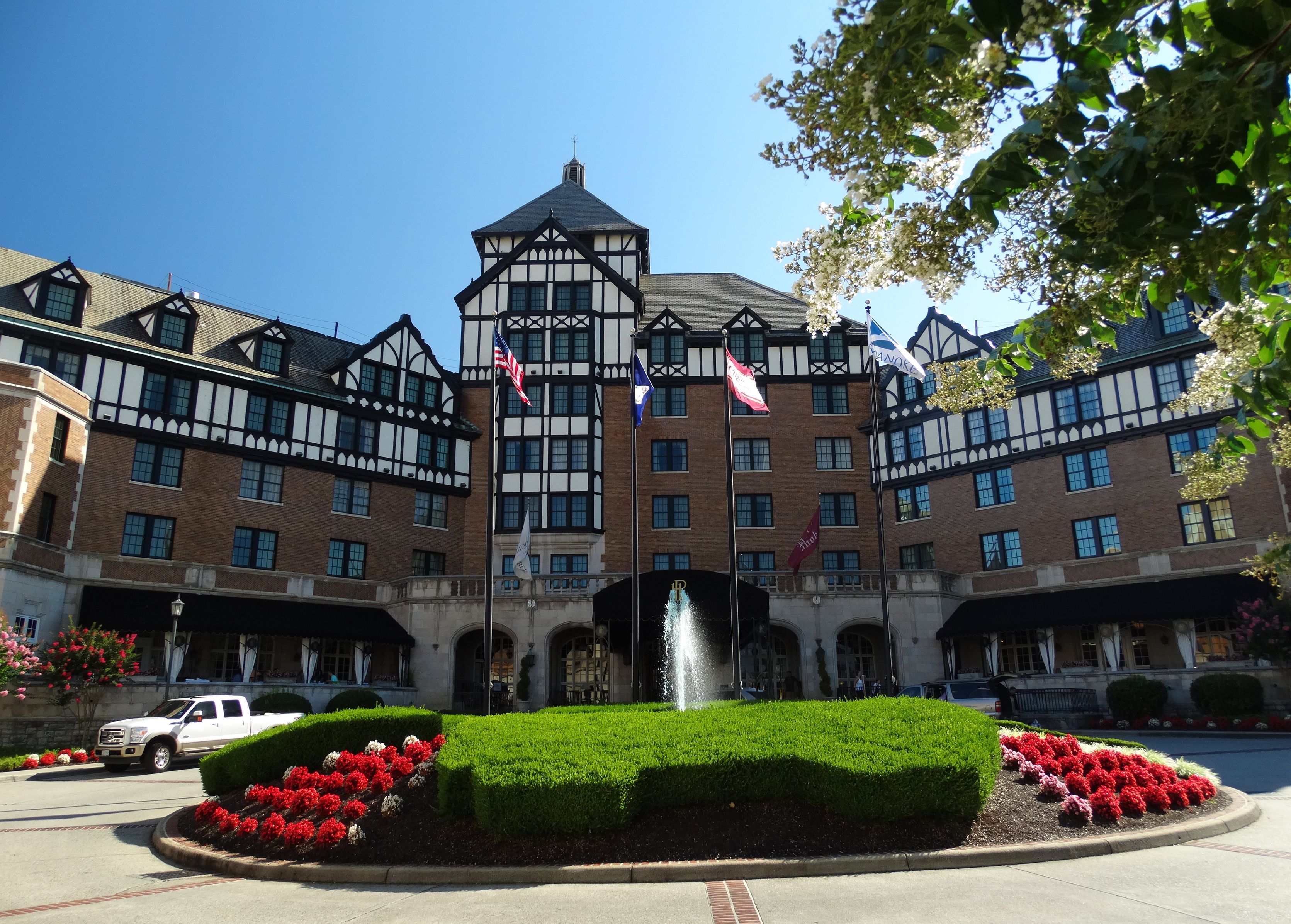 Un grand hôtel doté d’une fontaine centrale, de nombreux drapeaux et d’une façade symétrique de style Tudor.