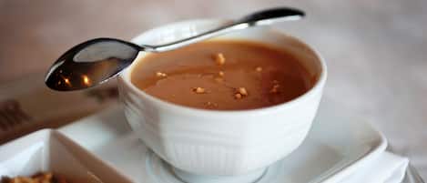 A white bowl of soup with a spoon on a white plate.