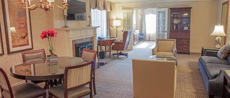 Une chambre d’hôtel comprenant un coin repas, un salon, une cheminée et une grande fenêtre.