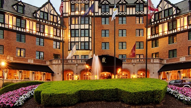 A large, historic building with multiple windows and a central tower. There are flags on poles and a fountain in the courtyard. - Hotel Roanoke & Conference Ctr, Curio Collection by Hilton  (Roanoke)