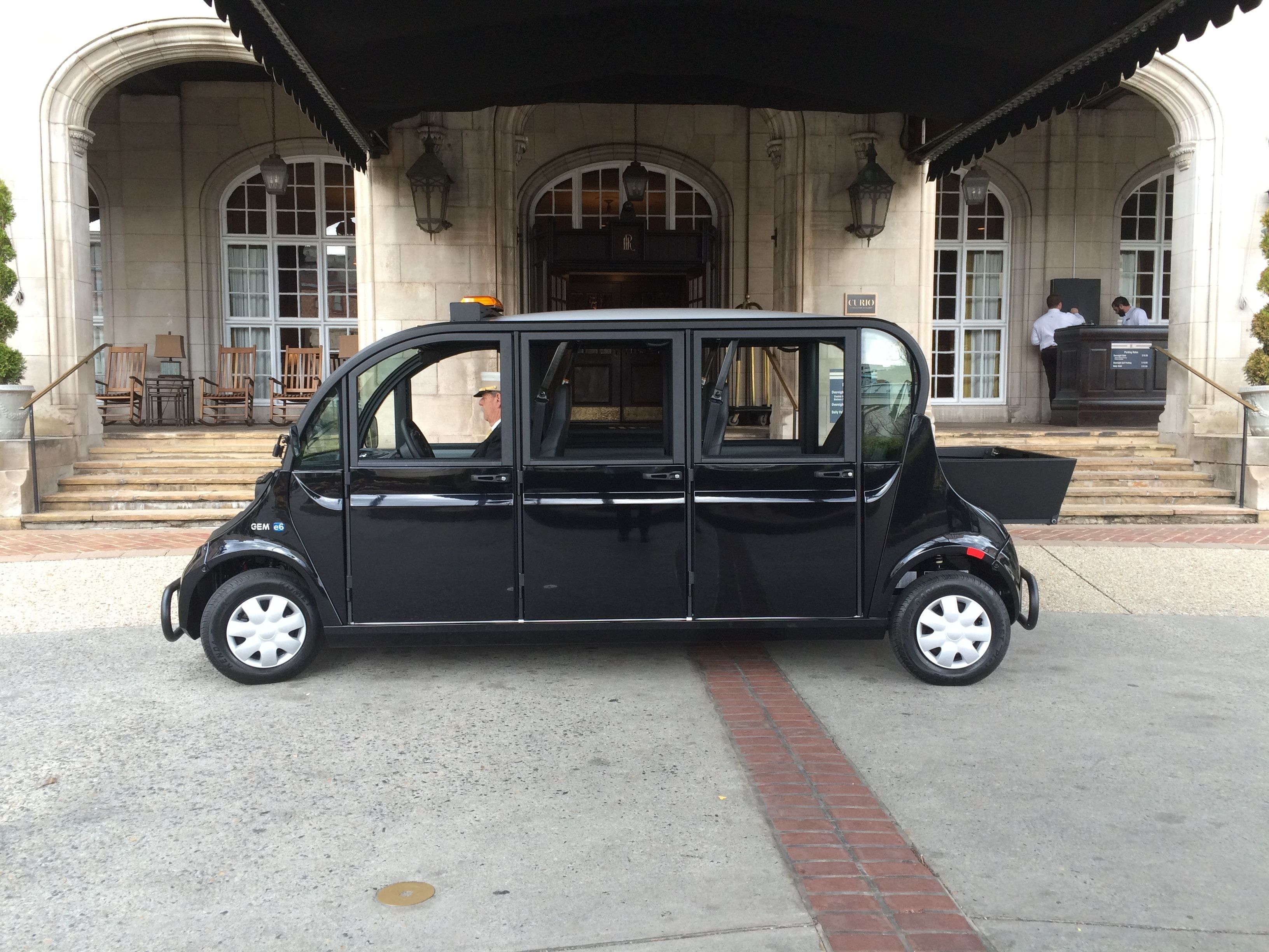 A black car parked in front of a building with arched windows and a covered entrance.