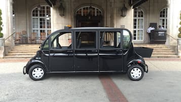 Um carro preto estacionado em frente a um edifício com janelas em arco e entrada coberta.