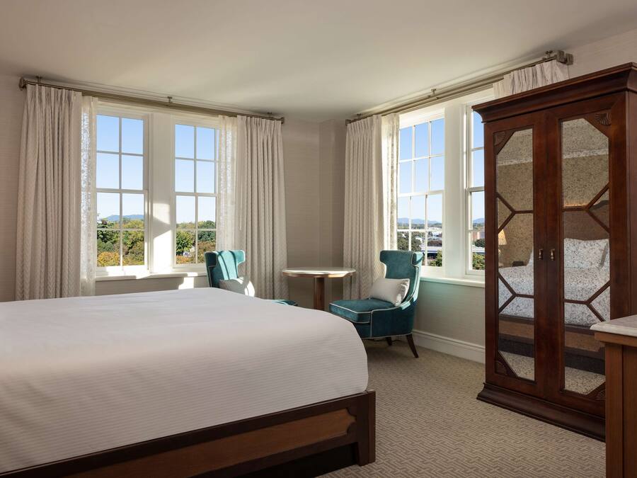 A hotel room with a large bed, two chairs, a small table, and a wardrobe.