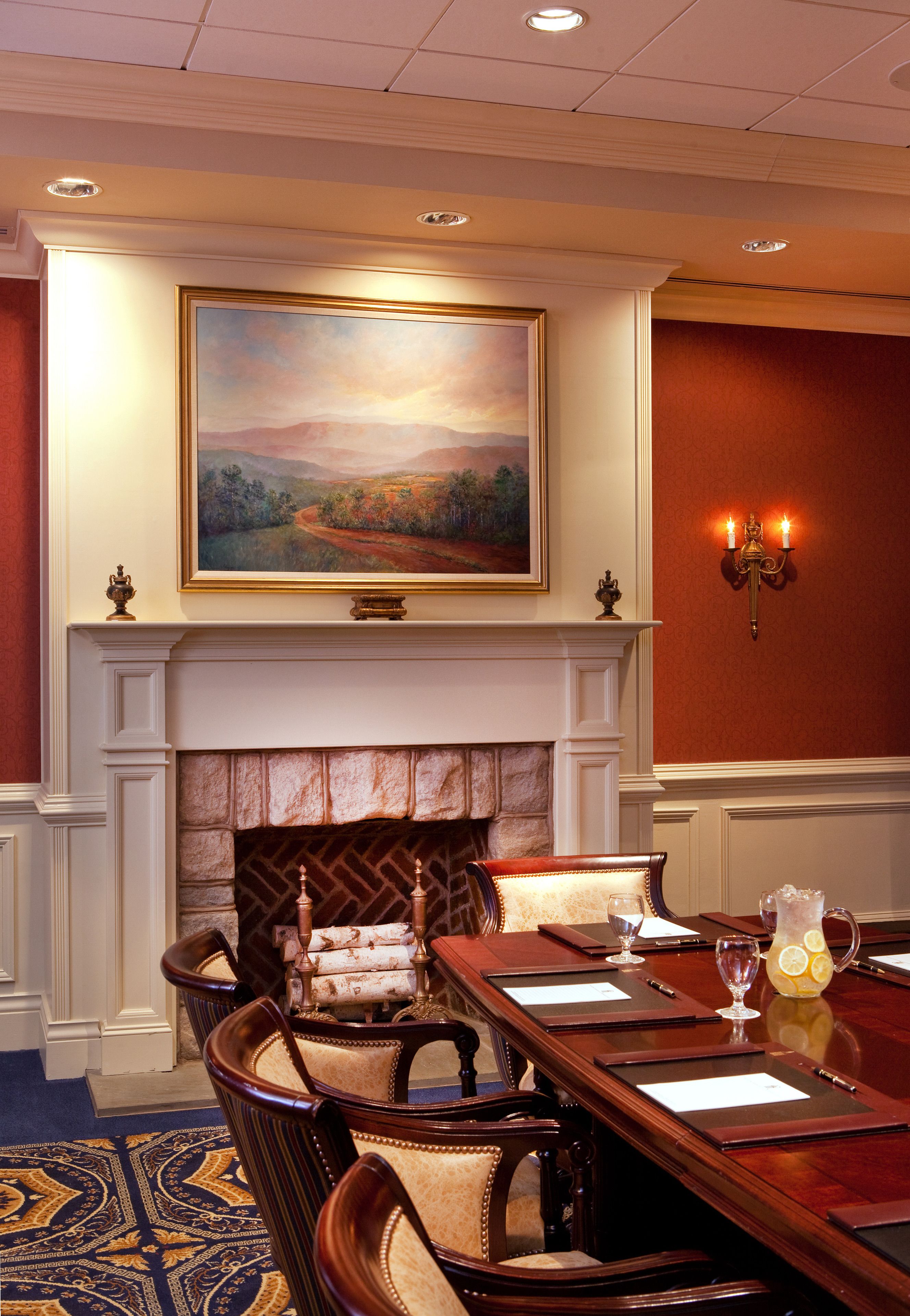 A conference room with a fireplace, a painting above it, and a table with chairs.