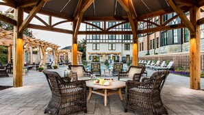 A covered outdoor seating area with wicker furniture and a central table, surrounded by stone walls and a pool. - Hotel Roanoke & Conference Ctr, Curio Collection by Hilton  (Roanoke)