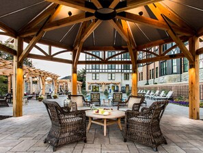 Relax in the shaded patio area with a wicker table and chairs, surrounded by exposed wooden beams and a vaulted ceiling.