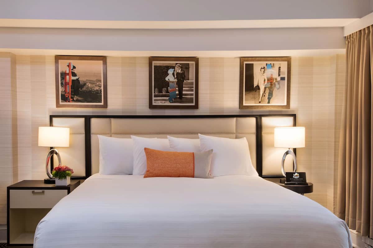A large bed with white linens, two nightstands with lamps, and three framed pictures on the wall.
