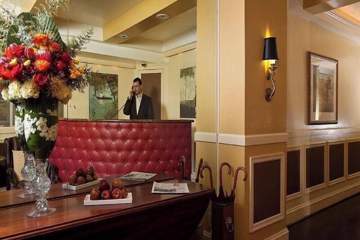 A reception area with a red upholstered bench, a vase of flowers, and a wooden desk with apples and papers.